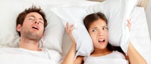 Bărbat care sforăie în somn, în timp ce partenera sa este deranjată – semn posibil de apnee obstructivă în somn.