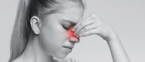Femeie cu durere intensă în zona nasului, simptom tipic al cefaleei rinogene provocate de afecțiuni ORL.