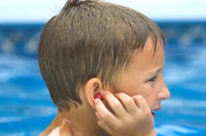 Copil cu dop de ureche roșu pentru prevenirea otitei de piscină, afecțiune comună în sezonul cald