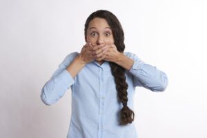 Femeie surprinsă în momentul în care își acoperă gura cu ambele mâini, exprimând surpriză sau jenă, ilustrând problema respirației urât mirositoare (halena).