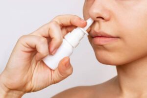 Femeie care aplică un spray nazal, ilustrând utilizarea corectă a spray-urilor nazale care nu provoacă dependență