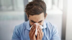Bărbat tânăr care își suflă nasul într-un șervețel, ilustrând problema nasului înfundat, cauze frecvente și soluții recomandate pentru marinari.