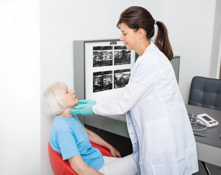 Medică examinând gâtul unei paciente în vârstă în cabinetul ORL, în timpul unei consultații clasice.