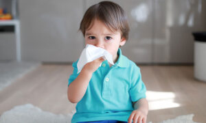 Copil cu nas înfundat, ținând un șervețel la nas, simbolizând soluțiile pentru nas înfundat la copii, incluzând remedii naturale și intervenții medicale.